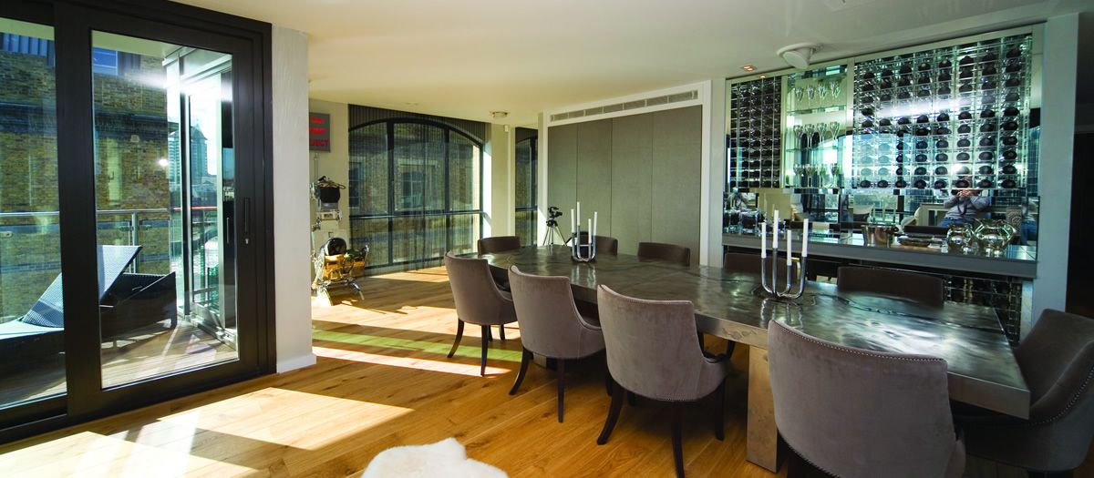 Bright entertaining/dining space with glass doors to a balcony, a long table with upholstered chairs, and a mirrored wine wall and bar.